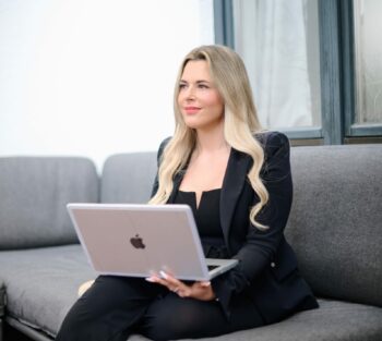 Laura Opferkuch, CEO von Hosta, sitzt auf einem Sofa und hat einen Laptop auf dem Schoß.