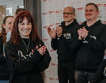 Ein paar Hosta Mitarbeitende in einheitlichen Pullovern stehen beisammen, klatschen Applaus und lachen.