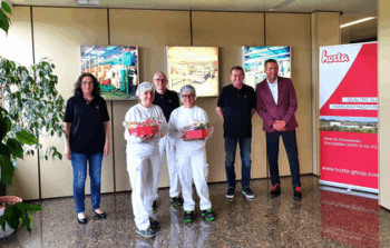 Zwei Hosta Mitarbeiterinnen in Laborkleidung und mit Präsentkörben stehen vor weiteren Mitarbeitenden und lächeln in die Kamera.